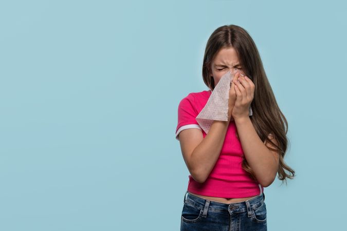 Girl sneezing into tissue to avoid spreading germs.