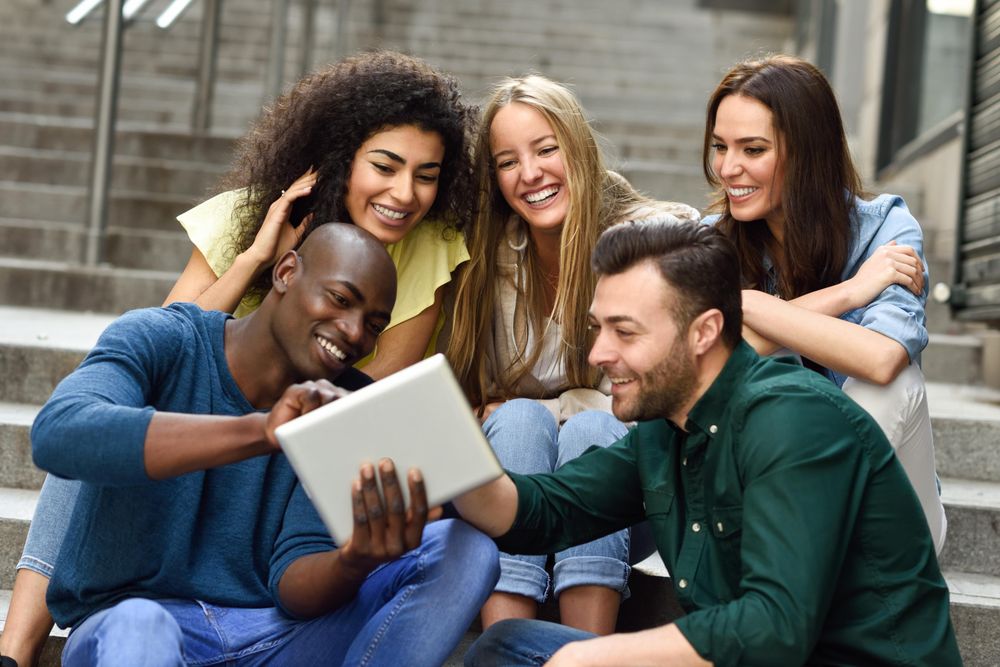Men and women focused on something on digital tablet while sitting on outdoor cement staircase