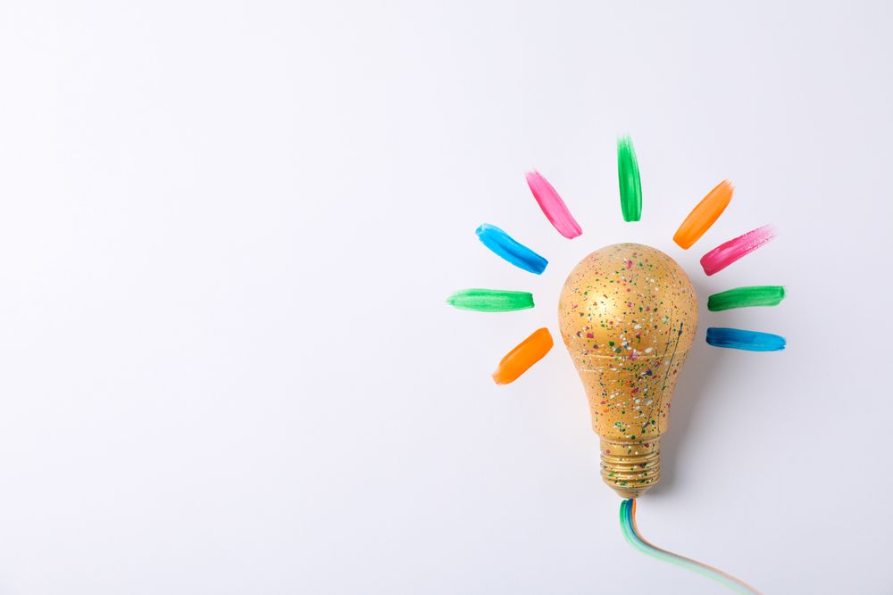 Light bulb with paint splatters on light background, space for text