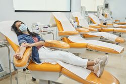 Woman in protective mask donating blood in modern clinic