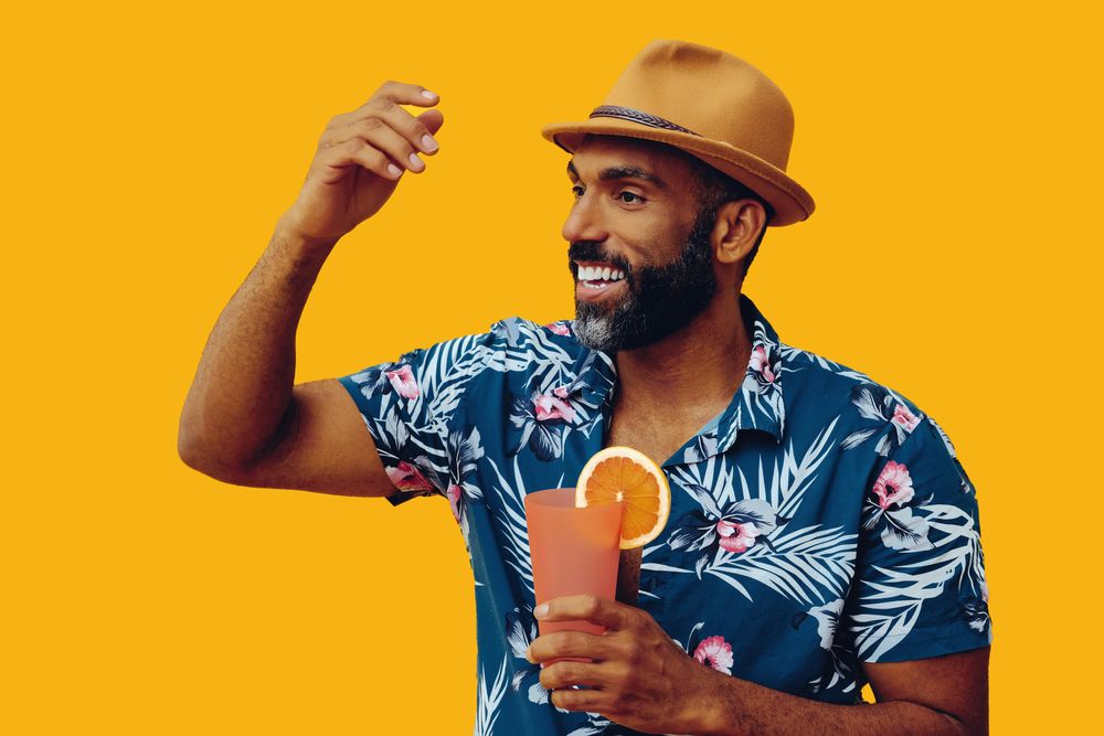 Smiling male holding a cocktail and talking while wearing colorful shirt with yellow background
