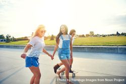 Happy female friends skateboarding on boardwalk bxkZM4