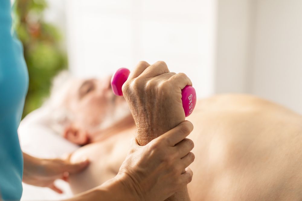 An older man receives a physiotherapy and rehabilitation session, using light weights,