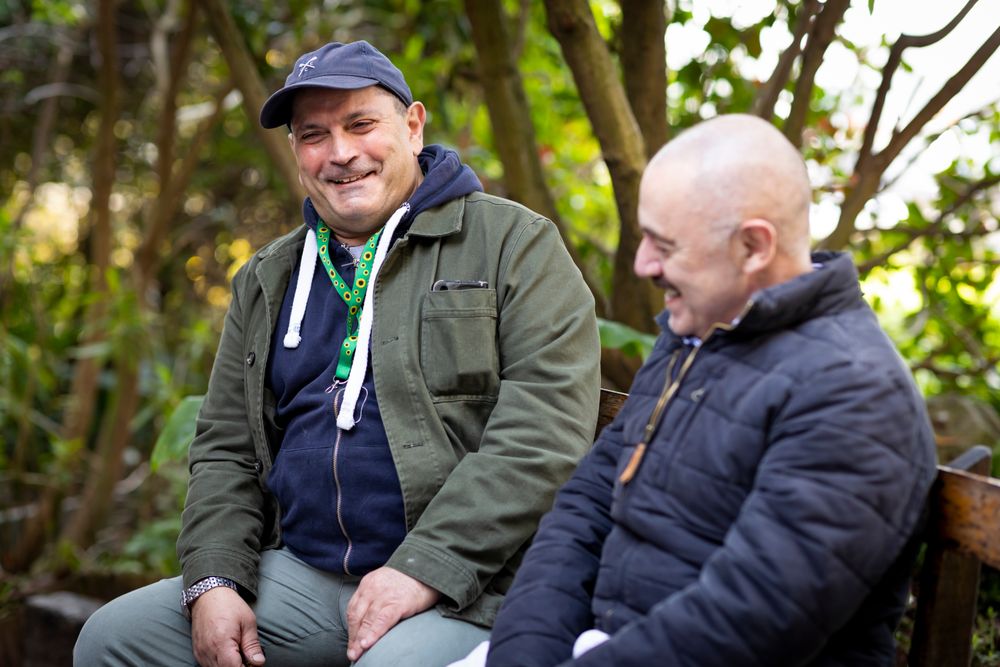 Two male friends chatting outside on a park bench