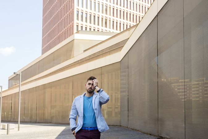 Young bearded man walking in front of building with hand to his head