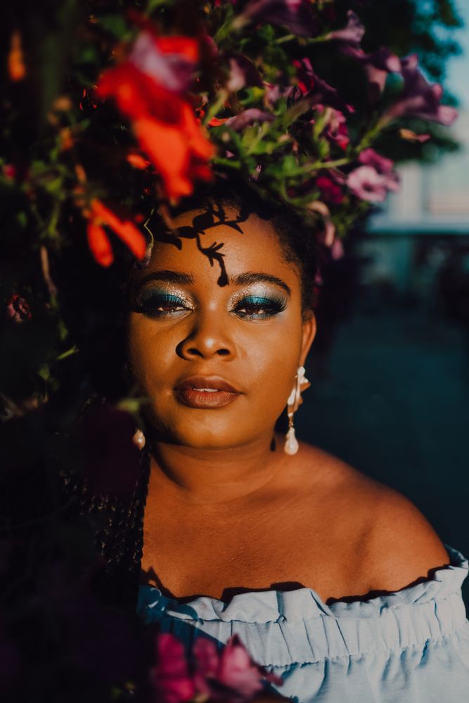 Joyful trendy Black woman standing beside blossomed tree