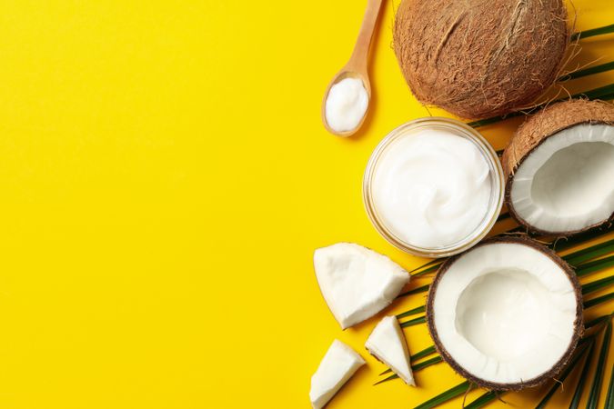 Coconut, cosmetics and palm branch on yellow background, top view