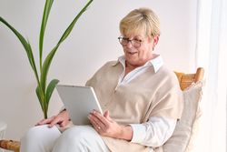 Smiling mature woman with tablet on wicker chair at home