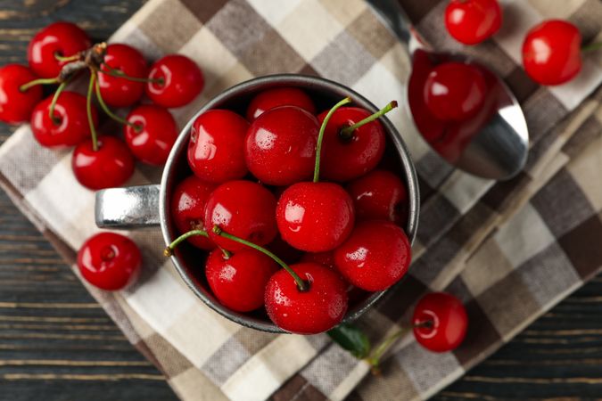 Towel and metal mug with cherry on wooden background, top view