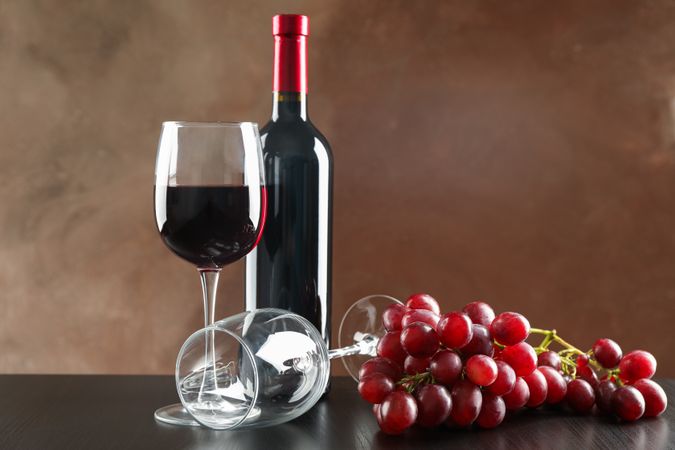 Grapes, bottle and glass with wine against brown background, copy space