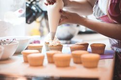 Cropped image of woman adding frosting to cupcake on tray