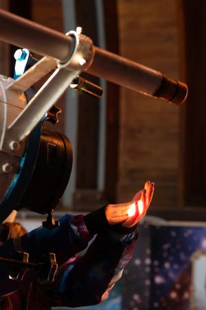 Gloved hand catching bright telescope light in observatory.