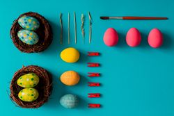 Bright Easter eggs, birds nests and clothes pins on cyan paper