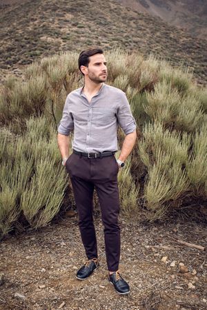 Stylish young man standing on hill near lush green bush
