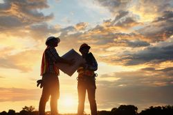 Two engineers holding a map and standing outdoor at sunset