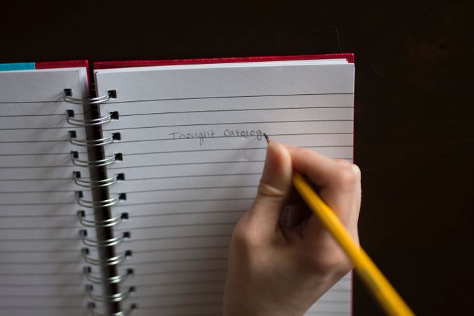 Cropped image of hand writing "Thought Catalog" on a notebook