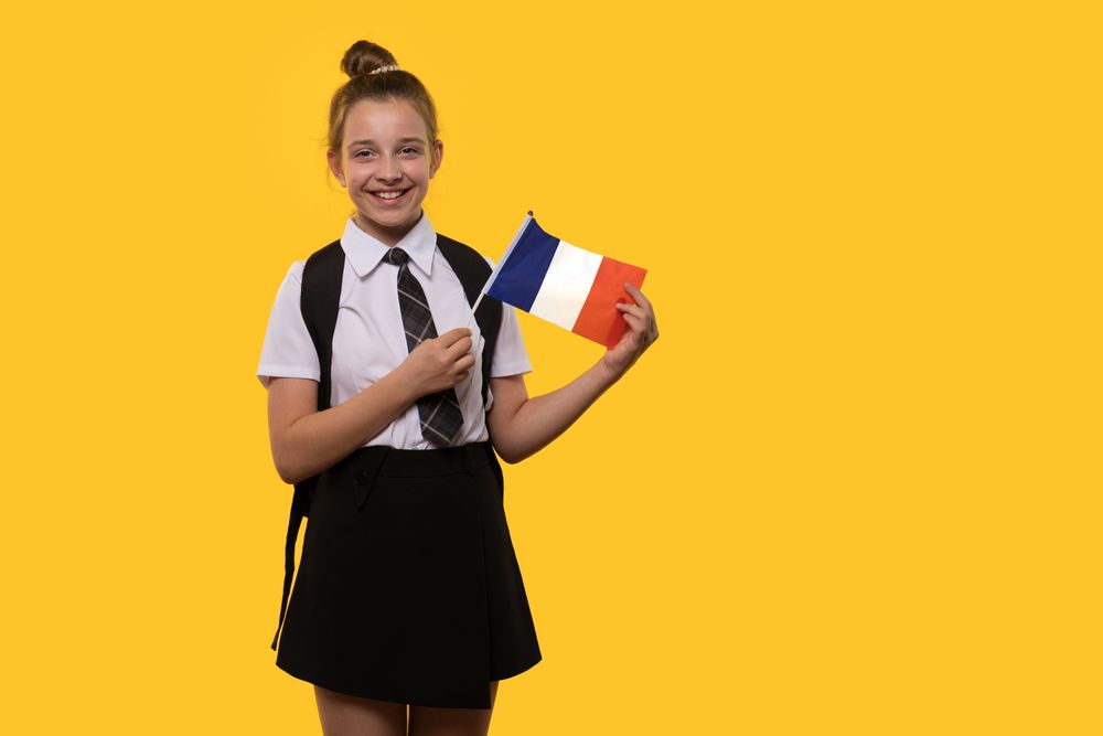 Schoolgirl holds the French flag while posing in uniform.