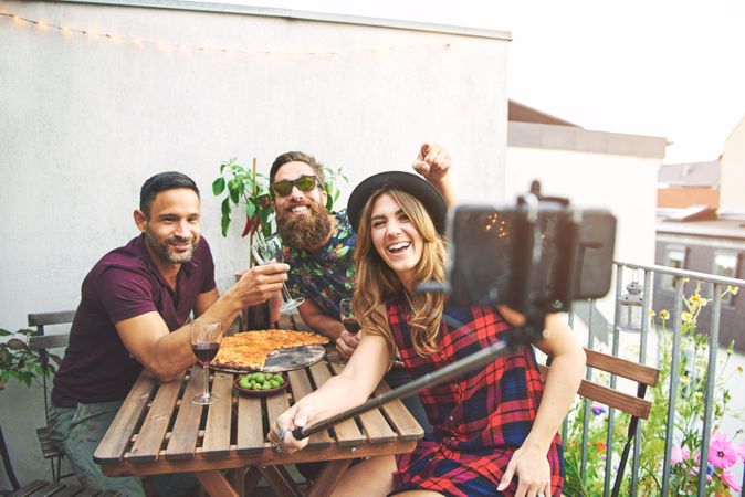 Group of friends smiling while taking selfie with pizza and wine outside