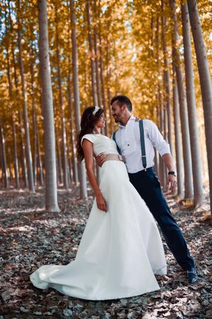 Newlywed husband and wife embracing in forest with tall poplar trees