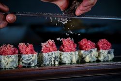 Crop person grating truffle on delicious uramaki sushi rolls with raw tuna