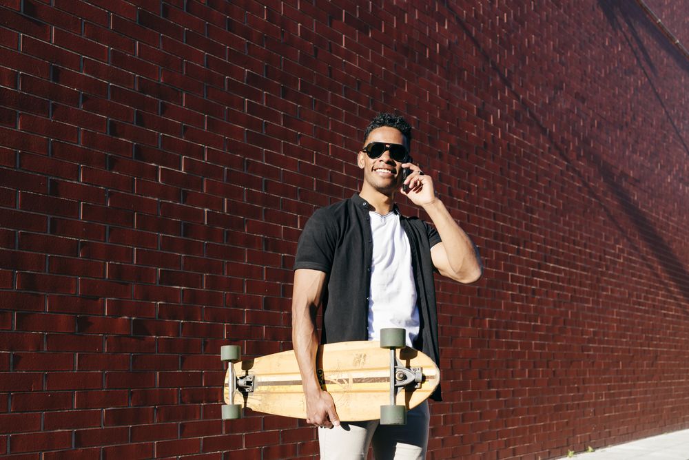 Young Black male with long board speaking on phone