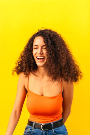 afro latina woman smiling and laughing portrait leaning on a yellow wall