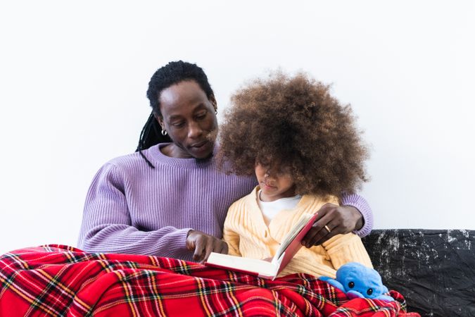 Black father reading book with daughter under plaid