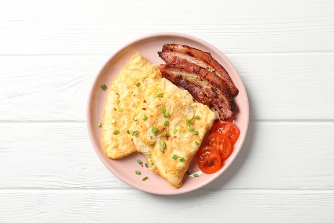 Breakfast of scrambled eggs and bacon on pink plate