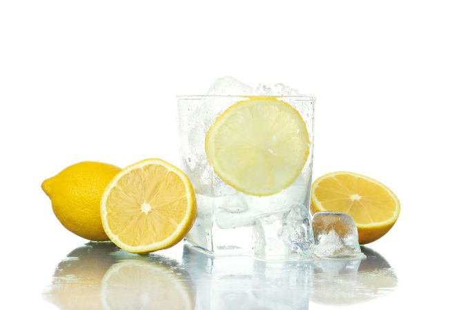 Rocks glass full of ice with lemon slice, surrounded by lemons halves