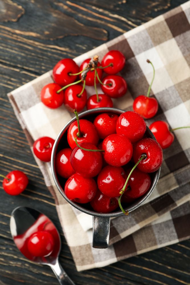 Towel and metal mug with cherry on wooden background, top view