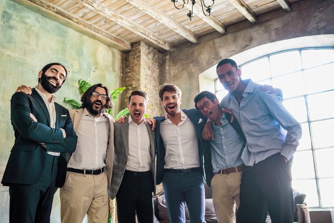 Diverse male colleagues hug each other while posing in office together