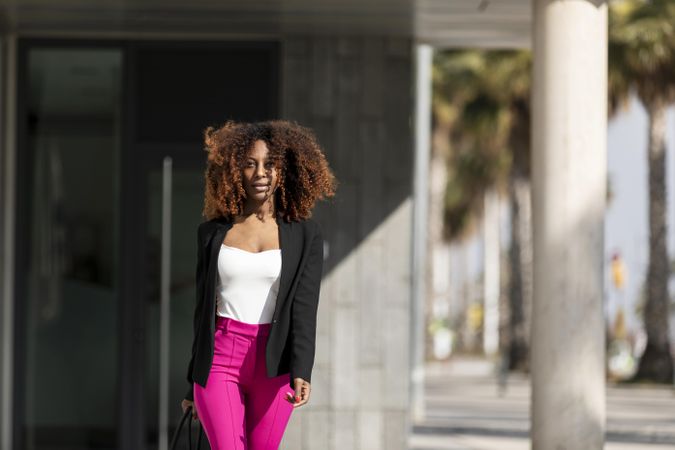 Black female in bright pink trousers with handbag standing outside