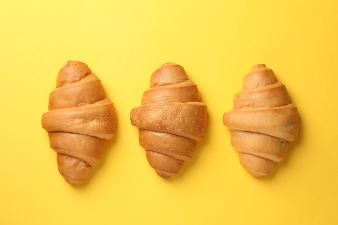 Baked croissants lined up on yellow background