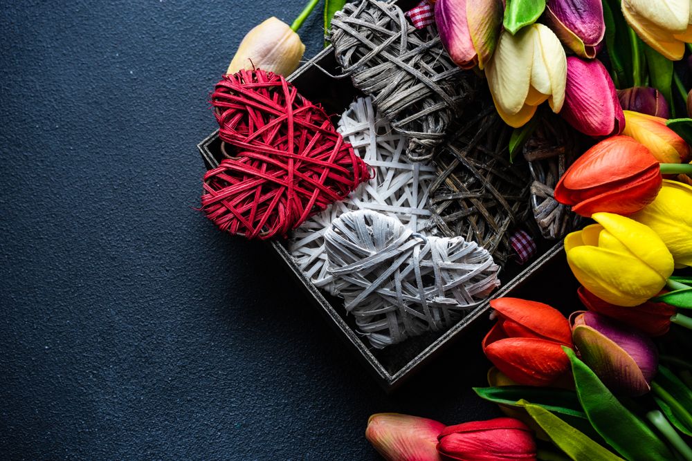 Box of thatched heart ornaments surrounded by fresh tulips