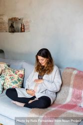 Pregnant woman happily holding her stomach on sofa 0Lz3X4
