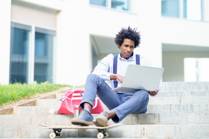 Man working on laptop and skateboard sitting on outdoors steps