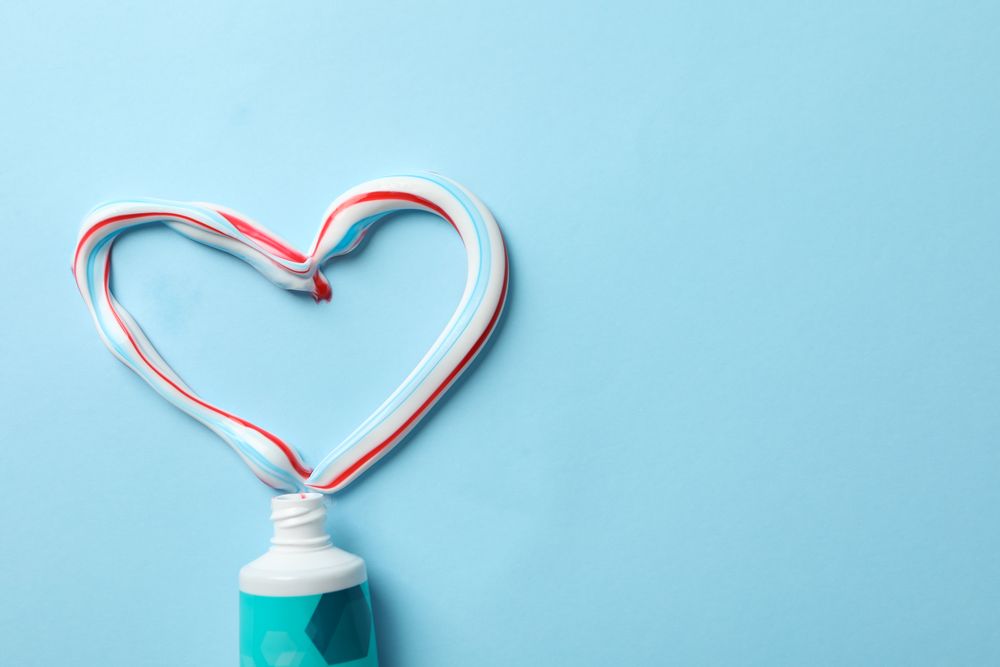 Heart made of toothpaste and tube on blue background, top view