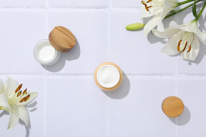 Jars with cream and lilies on light background, top view
