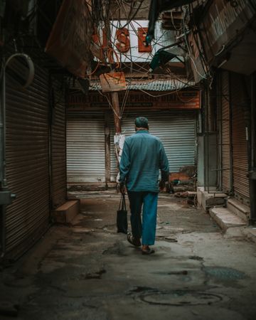 Back view of an older man in blue outfit walking in an alley