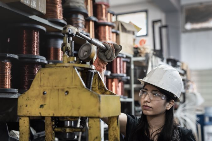 Woman wearing helmet and protective glasses working inside factory