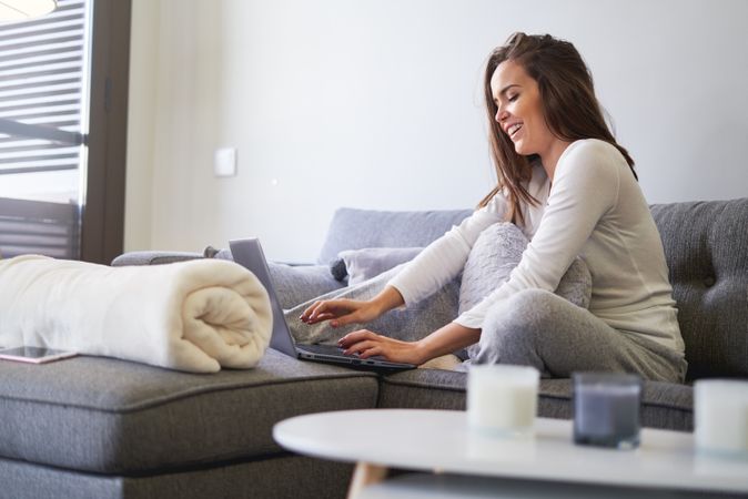 Smiling woman browsing on laptop and sitting on settee