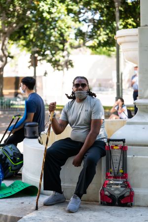 Los Angeles, CA, USA — June 16th, 2020: man with cane sitting on fountain looking at camera at rally