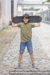 A teenage boy carrying skateboard behind head 0gX9oj