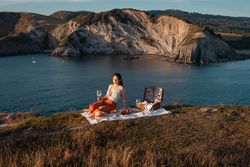 Woman with glass of drink on picnic mat looking at sea and mountains