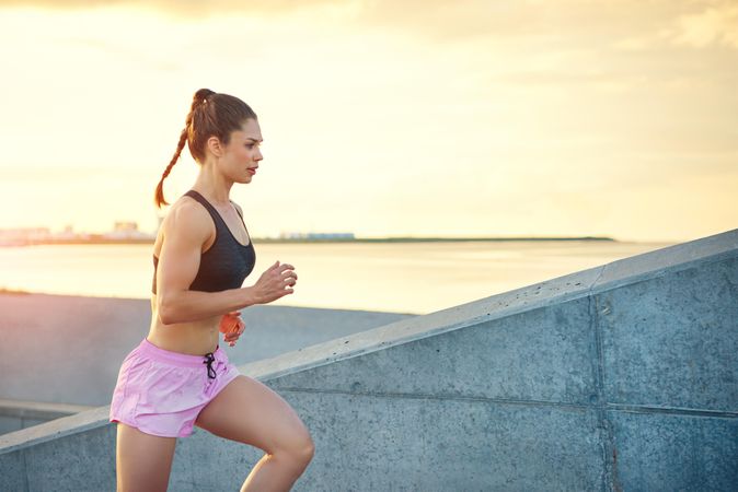 Athletic woman in sports bra and pink shorts running up concrete steps