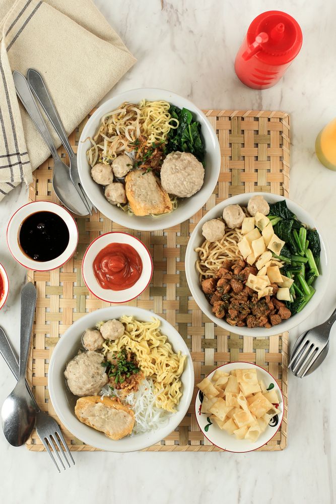 Top view of three bowls of noodles, fishcakes and vegetables