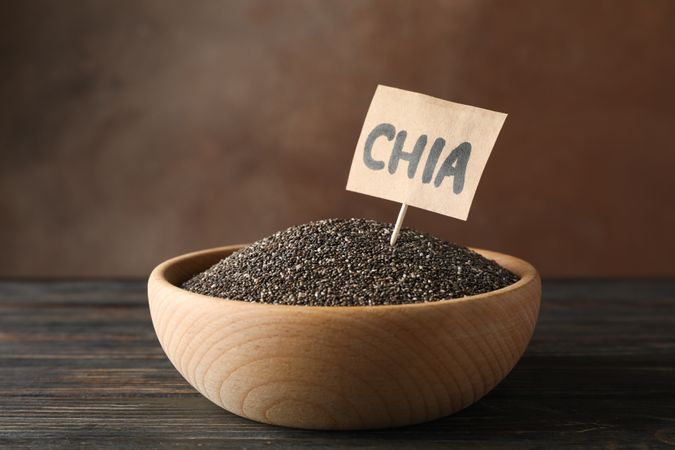 Wooden bowl and word Chia on wood background, copy space