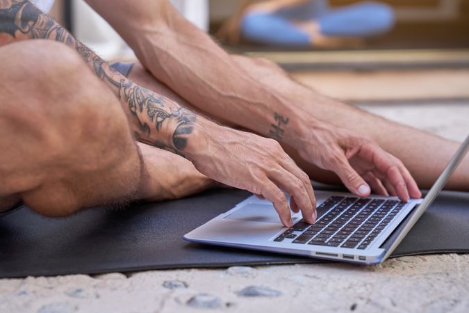 Crop tattooed man using laptop on mat