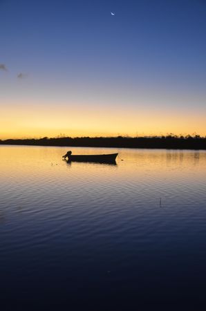 Silhouette of boat on still lake water during golden hour