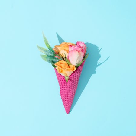 Pink ice cream cone with colorful flowers on pastel blue background